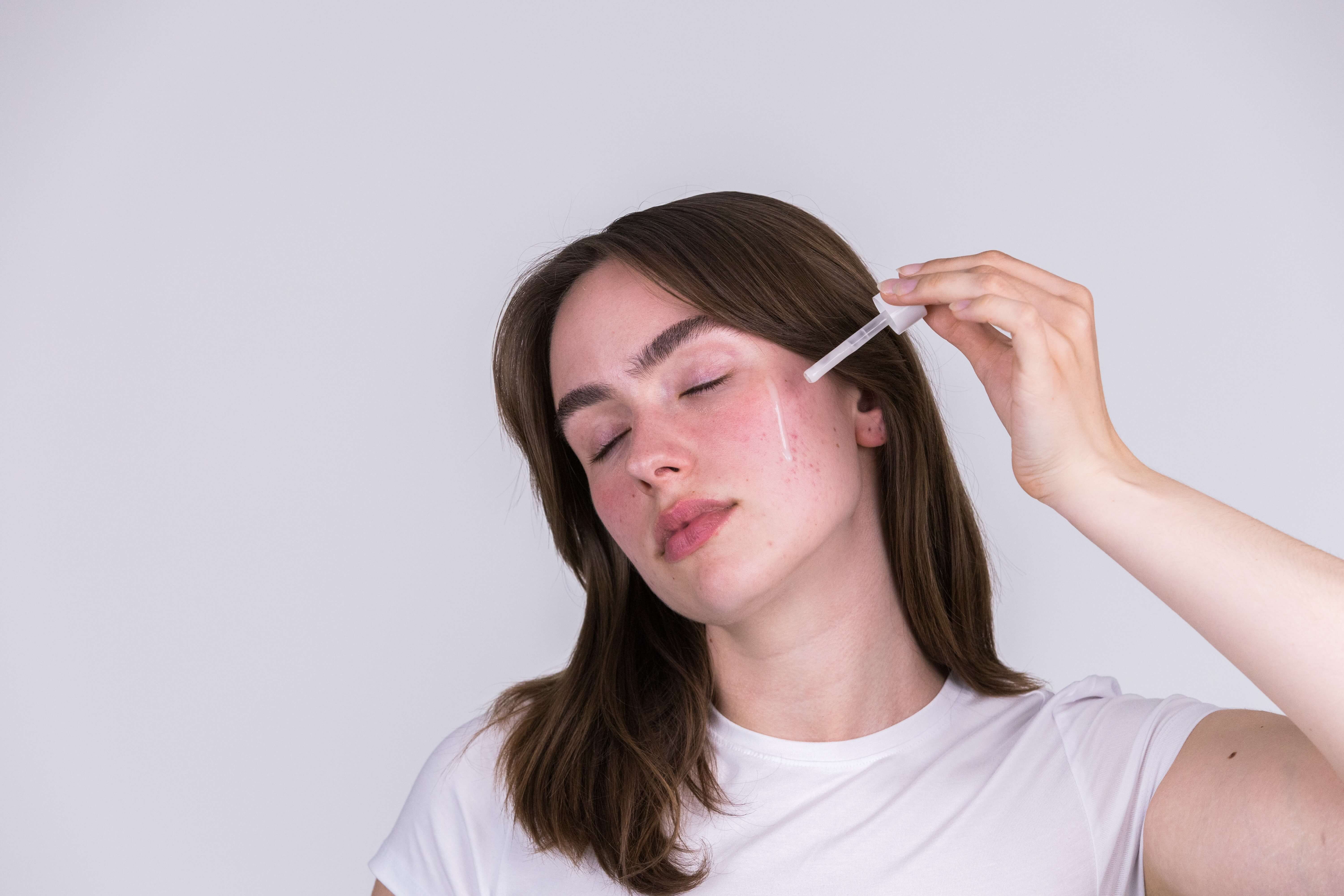 Frau, die sich mit einer Pipette ein Serum auf die Wange im Gesicht aufträgt