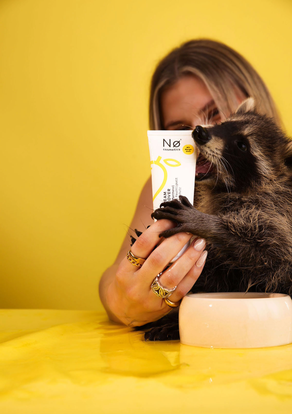 Handcreme mit Mangoduft, gehalten von einer Person und einem Waschbär 